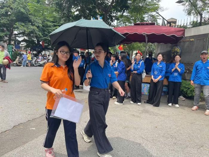Thanh niên tình nguyện che ô cho thí sinh tránh nắng di chuyển vào phòng thi.