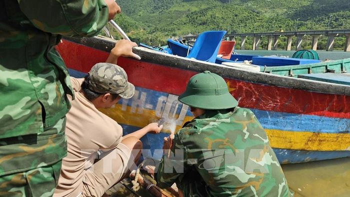 Lực lượng bộ đội biên phòng thành phòng Huế cùng ngư dân sơn biển số lên thân tàu theo đúng quy định. Ảnh: Mai Trang - TTXVN
