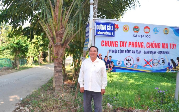 Ông Trương Ớ đứng trước pa-nô tuyên truyền thực hiện mô hình "Thôn không ma túy". Ảnh: KHẢI KHIÊM