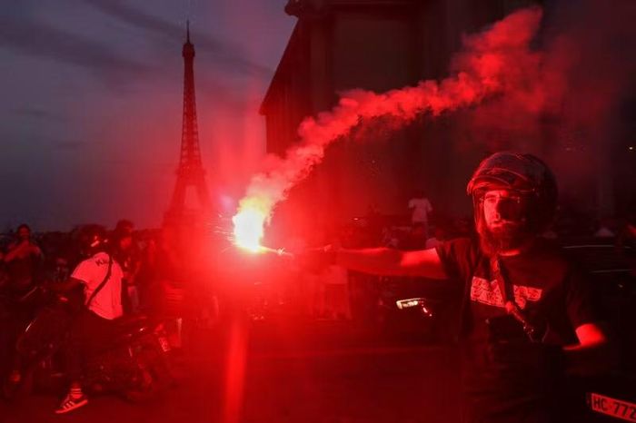 Hình ảnh một CĐV cầm pháo sáng với Tháp Eiffel phía xa. Sắc đỏ bao phủ nhiều khu vực tại Paris trong đêm PSG đánh bại Arsenal 4-3 ở loạt sút luân lưu để bảo vệ thành công ngôi vô địch Champions League.