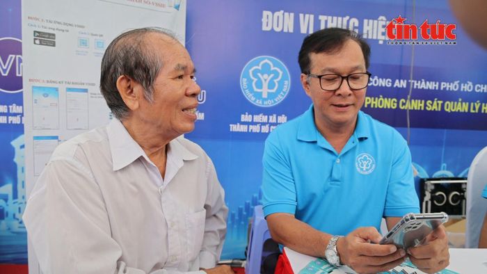 Ông Nguyễn Văn Chương (bên phải), Phó Giám đốc Bảo hiểm xã hội Cơ sở Chợ Lớn đang hướng dẫn người dân cài đặt và sử dụng ứng dụng VssID.