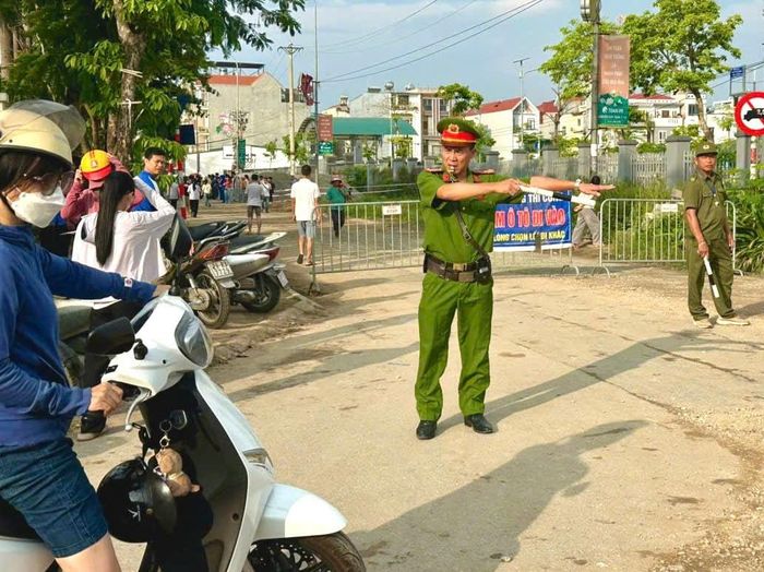 Đại úy Nguyễn Minh Hiếu, cán bộ Công an xã Đông Anh phân luồng, hướng dẫn người dân đỗ xe đúng nơi quy định tại cổng điểm thi Trường THCS Việt Hùng, xã Đông Anh. Ảnh: MK