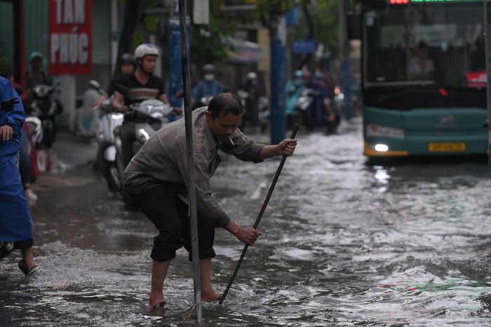  Nhiều người dân chủ động vớt rác tại các miệng cống, khơi thông dòng chảy, giúp nước rút nhanh hơn. Ảnh: PHẠM HẢI 