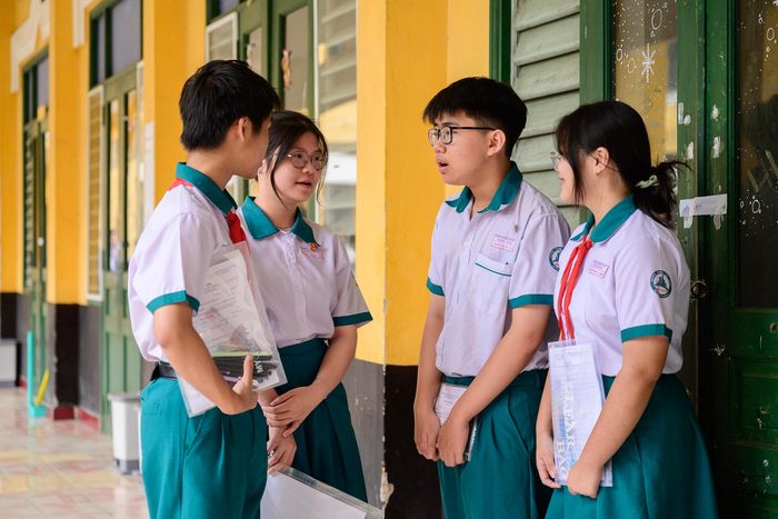 Trong lúc chờ vào phòng thi, Nguyễn Phi Long (nam sinh thứ hai từ phải qua), học sinh trường THCS Điện Biên, tranh thủ trò chuyện với bạn bè trước khi tập trung vào phòng thi. Dù học lớp chọn Toán, Long vẫn có phần lo lắng với môn học này. Em kỳ vọng đạt khoảng 8 điểm môn Ngữ văn, 9 điểm môn Toán và 7 điểm môn tiếng Anh để đậu lớp 10. Ngoài ra, nam sinh cho biết em đăng ký thi chuyên Lịch sử tại trường THPT chuyên Trần Đại Nghĩa. Thừa nhận phạm vi kiến thức của môn Lịch sử khá rộng, nam sinh chỉ đặt mục tiêu khoảng 3 điểm ở môn chuyên để trúng tuyển.
