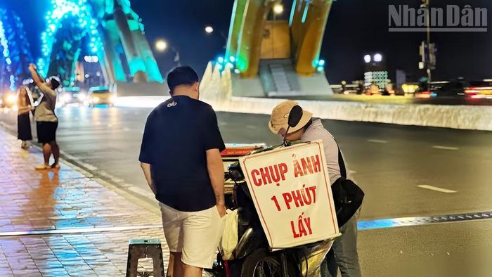 Chiếc xe máy gắn tấm bảng "Chụp ảnh 1 phút lấy" đã trở thành dấu hiệu quen thuộc của bà Đoàn Thị Thơ dưới chân Cầu Rồng suốt hơn 10 năm qua.