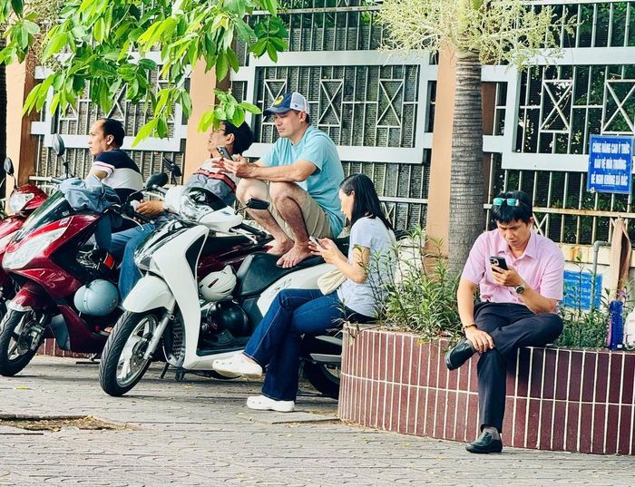 Các phụ huynh tận dụng bóng mát của hàng cây trước trường THPT Phú Nhuận để nghỉ ngơi chờ con thi. Ảnh: Hồ Lam