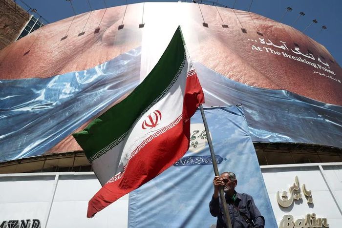 Một người đàn ông cầm cờ Iran gần một bảng quảng cáo có hình Tổng thống Mỹ Donald Trump và eo biển Hormuz, ở Tehran, Iran, ngày 30/5/2026. Ảnh: Reuters