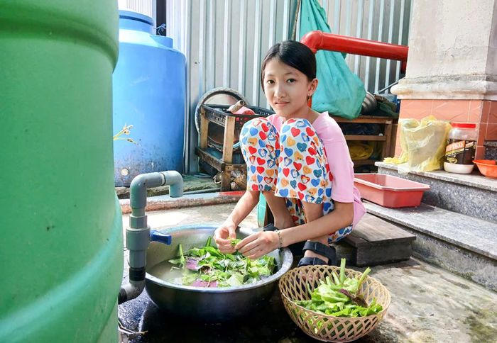 Con gái của chị Nguyễn Thị Hoàng Uyên tiếp mẹ nhặt rau sau giờ học. Ảnh: HẠNH CHÂU