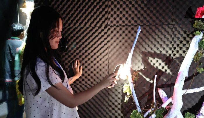 Du khách sử dụng ánh sáng từ điện thoại chiếu vào các bông hoa trong không gian “Âm thanh của gỗ” tại Nhà triển lãm Âm thanh, tạo nên những thanh âm và giai điệu khác nhau thông qua hệ thống cảm biến tương tác. Ảnh: Nguyễn Huy Thành - TTXVN