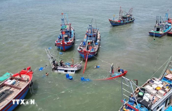 Các ngư dân tiến hành giữ thăng bằng thân tàu bằng việc cột buộc nhiều thùng nhựa kích thước lớn tại các vị trí xung quanh tàu cá và chờ thủy triều dâng cao đỉnh điểm sẽ tiến hành lai dắt vào bờ để sửa chữa. (Ảnh: Xuân Tiến/TTXVN)