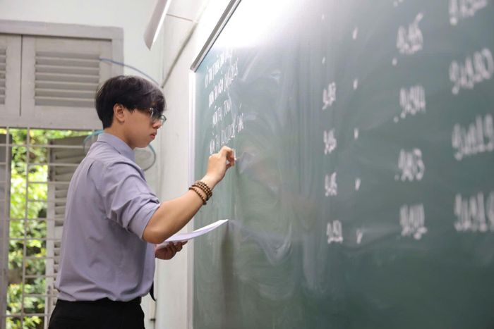 Một thầy giáo viết thông tin thời gian thi và môn thi lên bảng cho các thí sinh.