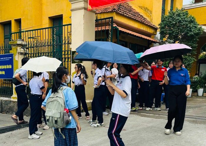 Các học sinh tình nguyện trường THPT Trưng Vương che ô cho các thí sinh khi trời đổ mưa chiều 1/6.