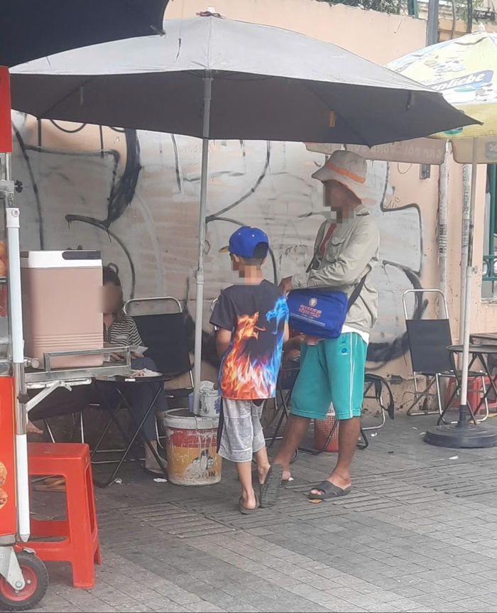  Một em nhỏ được một đàn anh dắt đi bán vé số khu vực Hồ Con Rùa, TP Hồ Chí Minh 