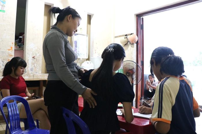 Mẹ nuôi Hồng Hiệp nhẹ nhàng chỉnh lại tư thế ngồi học cho một em nhỏ tại Làng Hòa Bình, từ những điều nhỏ nhất để hình thành thói quen học tập đúng cách và bảo vệ sức khỏe khi sử dụng thiết bị điện tử.