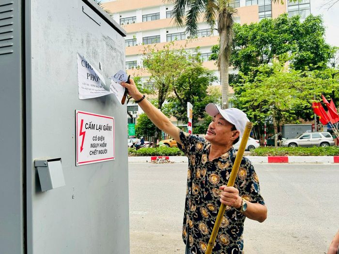 Cán bộ Mặt trận khu dân cư bóc dỡ quảng cáo rao vặt sai quy định dán trên tủ điện. Ảnh: Trần Oanh