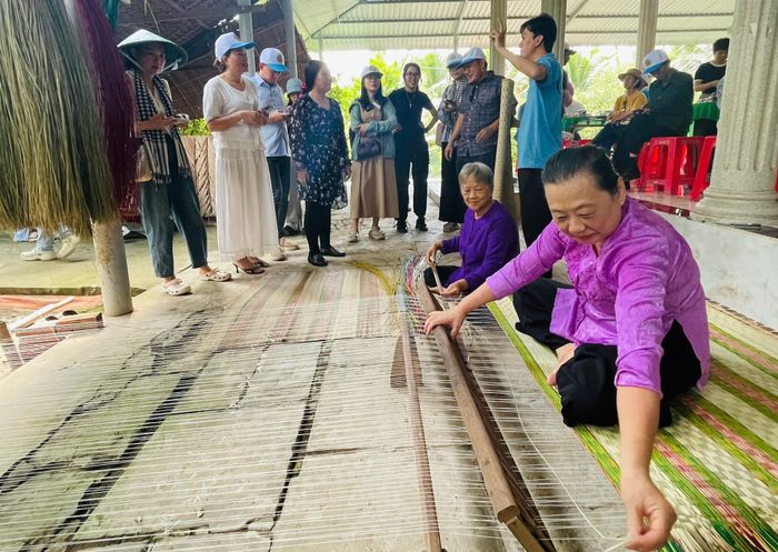 Du khách lắng nghe các quy trình làm ra sản phẩm tại làng nghề dệt chiếu thủ công bằng sợi cói nhuộm màu