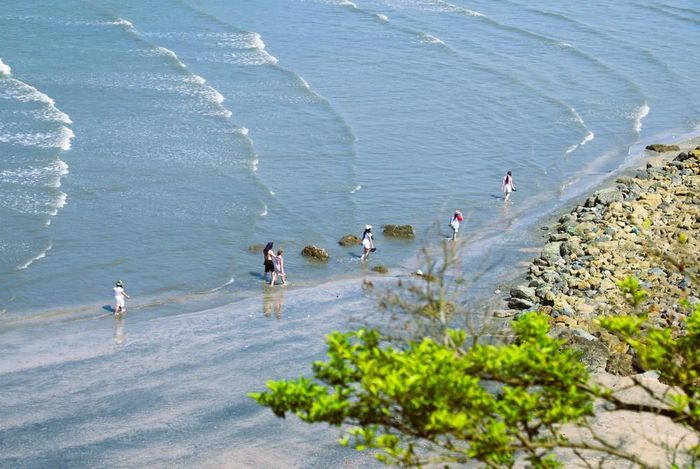 Du khách tản bộ dọc bãi biển bằng phẳng, quanh năm sóng vỗ dưới chân núi Mành Sơn, phía trước hang Mũi Trâu (xã Quỳnh Phú, tỉnh Nghệ An)