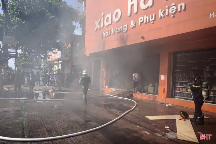 Khói đen từ bên trong cửa hàng thoát ra, gây khó khăn cho công tác cứu hộ. Lực lượng chức năng tiếp cận hiện trường từ tầng 2 nhà bên cạnh để dập lửa.