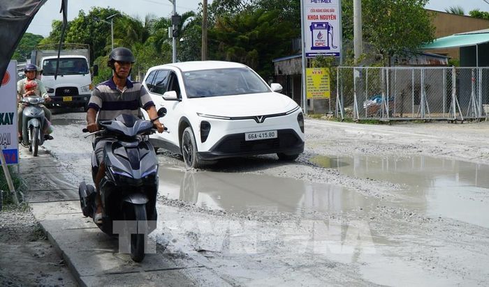 Người dân phải chạy xe gắn máy trên cống thoát nước để né những hố to bùn lầy trên Quốc lộ 30 đoạn qua ấp Gò Da, xã Tân Hồng. Ảnh: Nhựt An - TTXVN