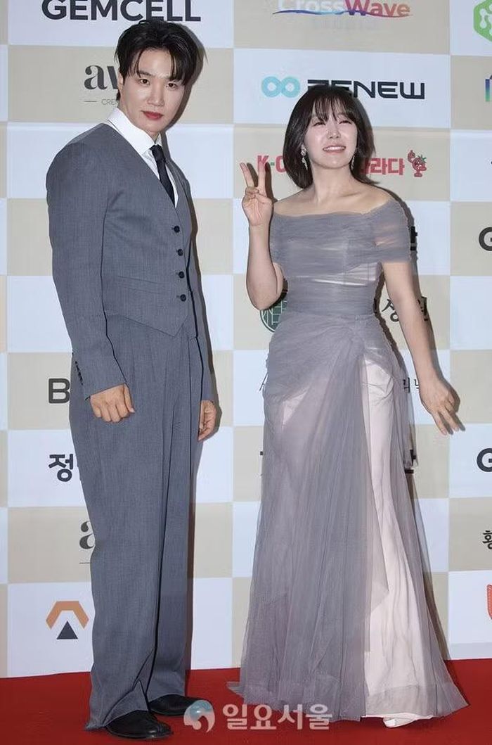 Kim Ki Ri xuất hiện với bộ suit xám ba mảnh, trong khi Ha Ji Young lựa chọn đầm dạ hội tông xám bạc với chất liệu xuyên thấu mềm mại. Cả hai cùng tạo dáng trên thảm đỏ trước giờ làm MC buổi trao giải.