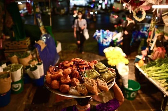 Một người bán hàng rong mang khay đầy ắp các món ngon đi dọc con hẻm tại chợ Pak Khlong Talat ở Bangkok, Thái Lan. Ảnh: Getty.