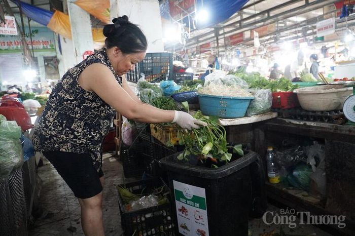 Tiểu thương Nguyễn Thị Liên phân loại rác tại quầy, gom các loại rau, vỏ dứa, gốc rau...vào thùng rác hữu cơ