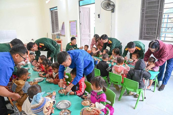 Cán bộ, đội viên Đội Sản xuất và xây dựng cơ sở số 5, Đoàn 313 cùng các cô giáo Điểm trường Hoàng Lao Chải chăm sóc học sinh trong bữa cơm bán trú.