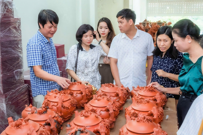 Nghệ nhân Đỗ Tùng Mậu cùng nghệ nhân Trần Thị Lý (thứ 2 từ trái sang) giới thiệu về sản phẩm gốm son đỏ. Ảnh: NVCC