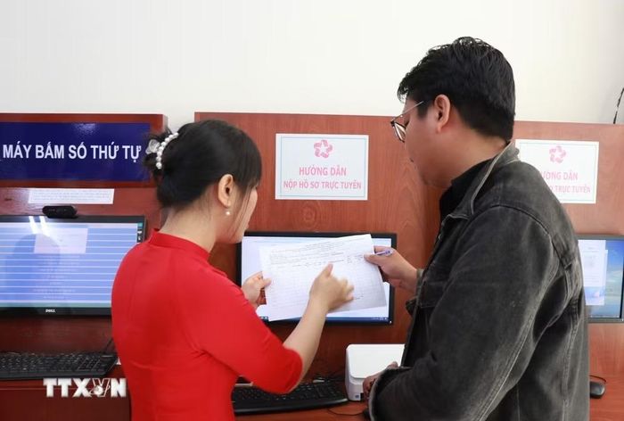 Cán bộ bán chuyên trách hướng dẫn người dân các thủ tục lấy số, ghi biểu mẫu tại trung tâm hành chính công phường Nha Trang, tỉnh Khánh Hòa trong ngày làm việc đầu tiên 1/7. (Ảnh: Phan Sáu/TTXVN)