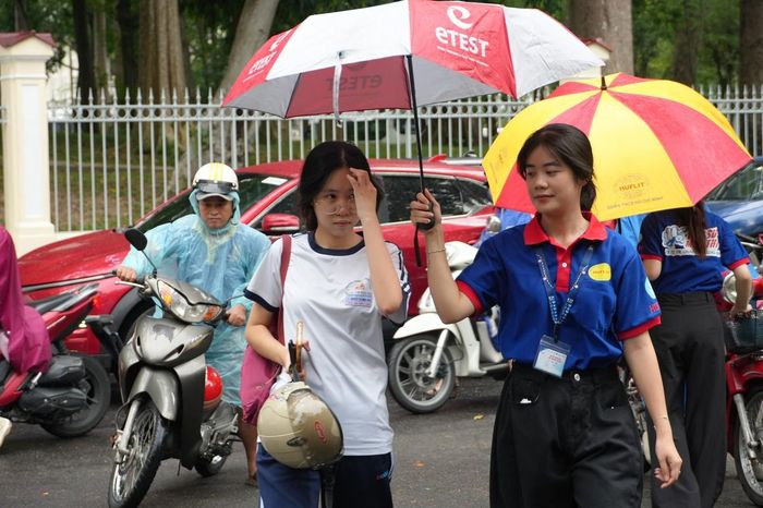 Lực lượng tình nguyện viên hỗ trợ che dù cho thí sinh và phòng thi.