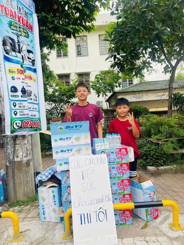 Hai em học sinh Trường THCS Cổ Đô cùng gia đình tặng nước uống và sữa miễn phí tới các anh chị thí sinh tại cổng Trường THPT Ngô Quyền - Ba Vì.