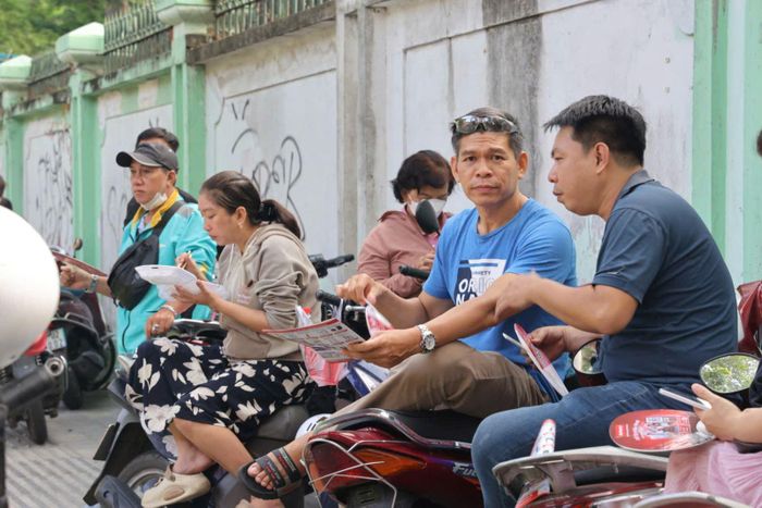 Sau khi đưa con vào điểm thi, một số phụ huynh mới trang thủ ăn sáng và ngồi chờ con bên ngoài trường thi.
