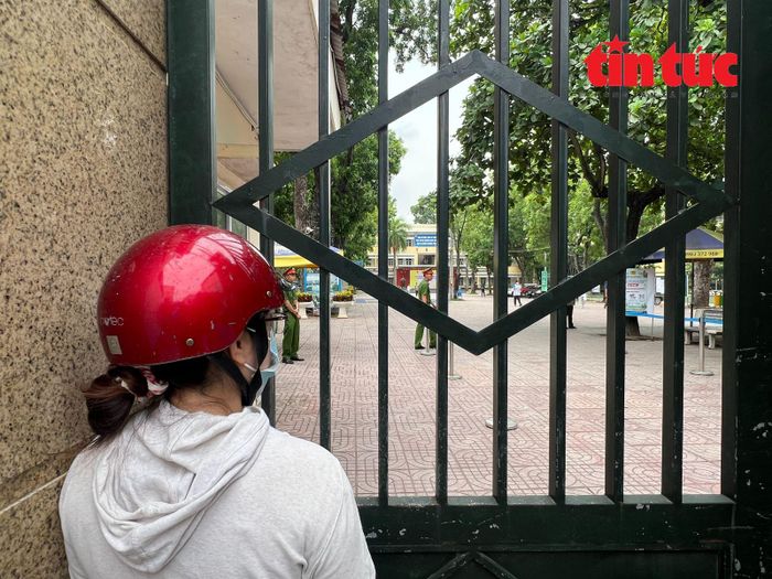 Một phụ huynh đứng sát cổng trường, ánh mắt hướng về khu vực phòng thi, chờ đợi con.