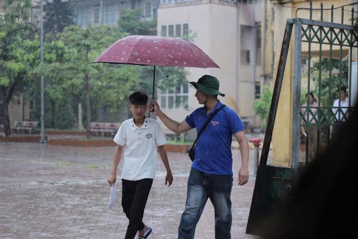 Một tình nguyện viên tận tình che ô cho thí sinh, đảm bảo các em không bị ướt mưa để giữ sức khỏe và tinh thần tốt nhất cho buổi thi chiều 11/6.