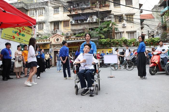 Một thí sinh ngồi xe lăn được đội tình nguyện viên đưa vào điểm thi. Ảnh: Vân Đức