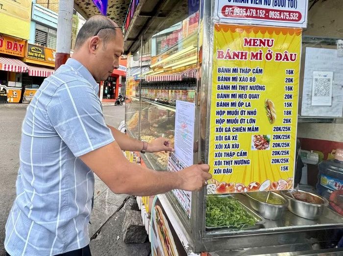  Đoàn công tác dán áp phích tuyên truyền và bảng cam kết thực hiện các quy định về an toàn thực phẩm tại cơ sở kinh doanh bánh mì trên đường Ngô Mây. Ảnh: Thảo Khuy 