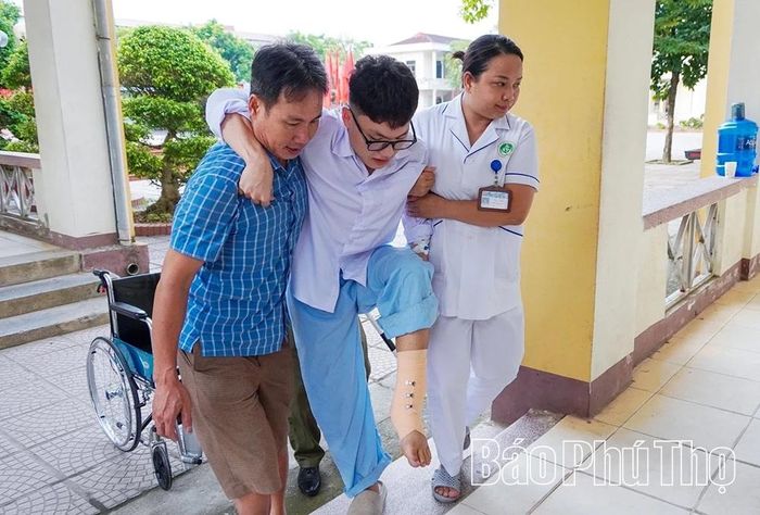 Với sự hỗ trợ của người thân và cán bộ Trung tâm Y tế khu vực Cẩm Khê, em Lê Công Sơn di chuyển vào phòng thi sau ca phẫu thuật chân trái, thể hiện quyết tâm không bỏ lỡ Kỳ thi tốt nghiệp THPT năm 2026.