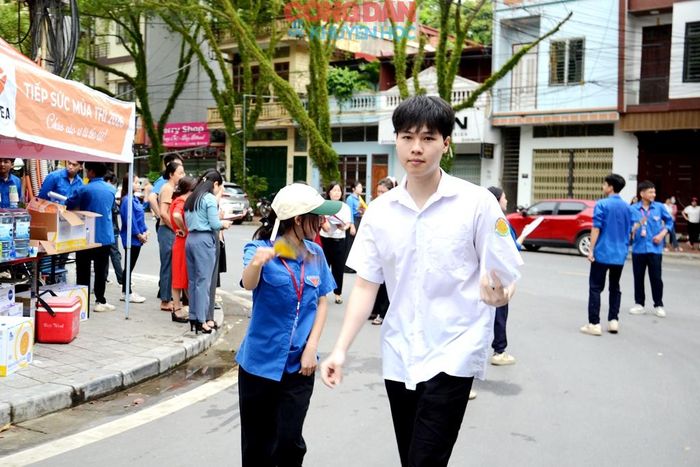 Một thí sinh được đoàn viên thanh niên phường Cam Đường hướng dẫn đến làm thủ tục vào phòng thi. Ảnh: Quốc Hồng