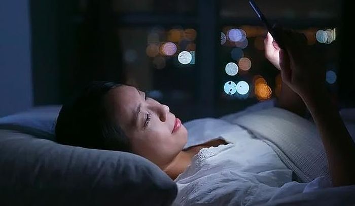 Tắt đèn rồi nằm xem điện thoại trước khi ngủ là thói quen xấu nhiều người mắc phải. Ảnh MH