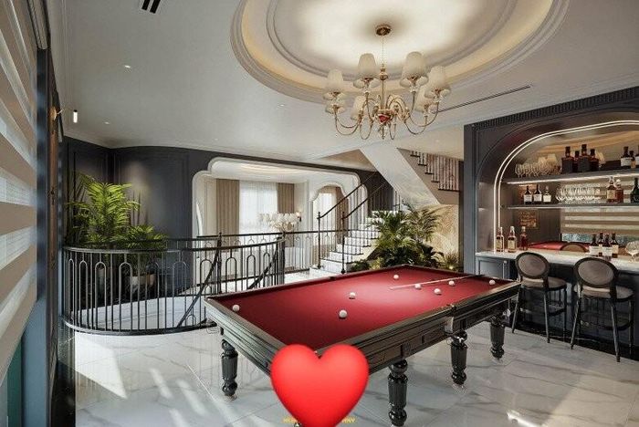 Không gian tầng 2 mở ra là khu giải trí. Nơi đó đặt một bàn billiards với mặt đỏ đô nổi bật, mang đậm nét quý tộc cổ điển phương Tây. Ngay bên cạnh là quầy bar mini với hệ tủ rượu âm tường được thiết kế vòm mềm mại, kết hợp đèn LED hắt sáng làm nổi bật bộ sưu tập rượu và ly pha lê.