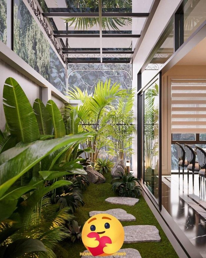 Ngay cạnh khu bếp là một mảnh vườn nhỏ phủ đầy cây xanh. Lối đi lát đá tự nhiên dẫn dọc theo hành lang bên hông nhà, tạo cảm giác như bước vào một khu vườn resort thu nhỏ. Thảm cỏ xanh mướt trải đều nền, xen kẽ với những bụi cây lá lớn như chuối cảnh, cau cảnh,... giúp nơi này càng tươi mát hơn.
