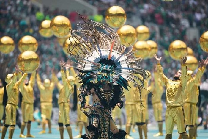 Một nghệ sĩ trong trang phục lấy cảm hứng từ văn hóa bản địa Mexico xuất hiện giữa dàn diễn viên cầm những quả cầu màu vàng, tạo nên điểm nhấn thị giác ấn tượng.
