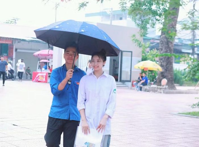 Nữ sinh được tình nguyện viên che ô vào tận phòng thi do đầu giờ sáng 12/6 có mưa nhỏ.
