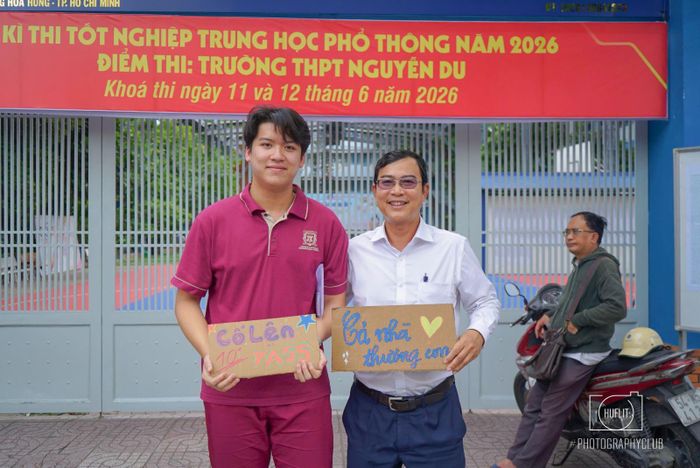 Một phụ huynh vui vẻ chụp ảnh bên con trai trước khi vào phòng thi với tấm bảng cỗ vũ đáng yêu.