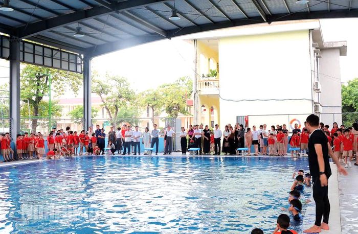 Các đại biểu và các em học sinh tham gia khai mạc lớp dạy bơi miễn phí tại bể bơi Trường Tiểu học Đồng Phong.