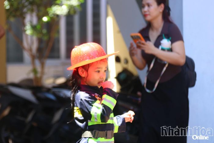 Một chiến sĩ nhí mặc đồng phục đang quan sát "đồng đội" thực hành chữa cháy bằng vòi phun nước.