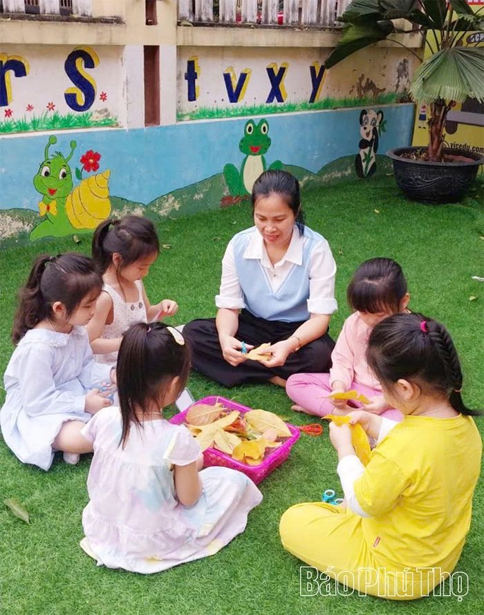 Cô giáo Trường Mầm non Hoa Hồng hướng dẫn các bạn nhỏ làm đồ chơi từ chiếc lá rụng trong sân trường.