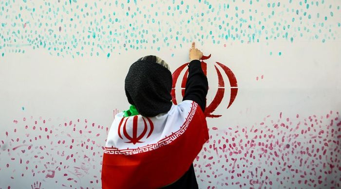 Một người phụ nữ đặt dấu vân tay của mình lên biểu ngữ có hình quốc kỳ Iran vào tháng 5. Ảnh: IQNA