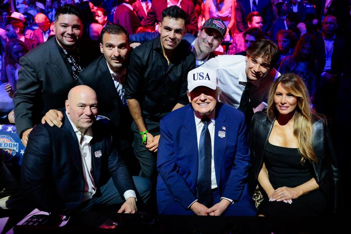 Tổng thống Mỹ Donald Trump mỉm cười khi ngồi cạnh Đệ nhất phu nhân Melania Trump và Giám đốc điều hành UFC Dana White trong lúc chụp ảnh cùng các khách mời khác tại sự kiện UFC Freedom 250 trên bãi cỏ phía Nam Nhà Trắng.
