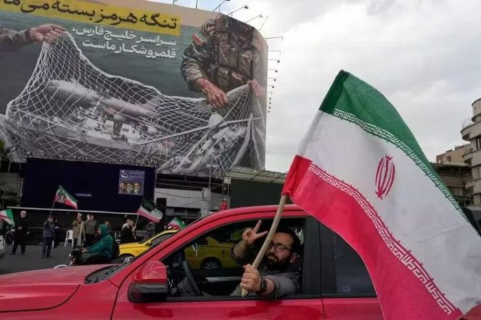 Một người dân Iran cầm quốc kỳ, giơ tay với biểu tượng "Victory" (Chiến thắng). (Ảnh: AP)